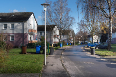 Foto einer Straße in einer Wohnsiedlung, Mehrfamilienhäuser, nasser Asphalt bei Sonnenschein