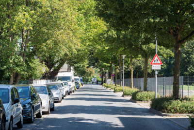 Straße mit parkenden Autos links und Hinweisschild auf spielende Kinder
