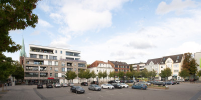 Marktplatz mit parkenden Autos, in Hintergrund hohe Gebäude