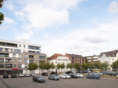 Marktplatz mit parkenden Autos, in Hintergrund hohe Gebäude