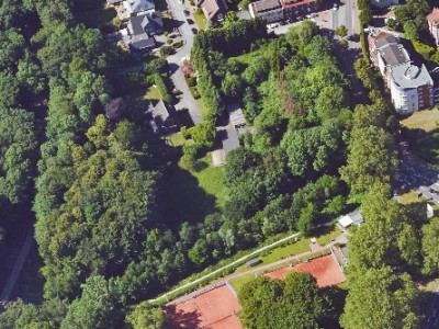 Luftaufnahme eines Stadtgebiets mit Häusern, Bäumen, einem Asche-Sportplatz und Fußwegen